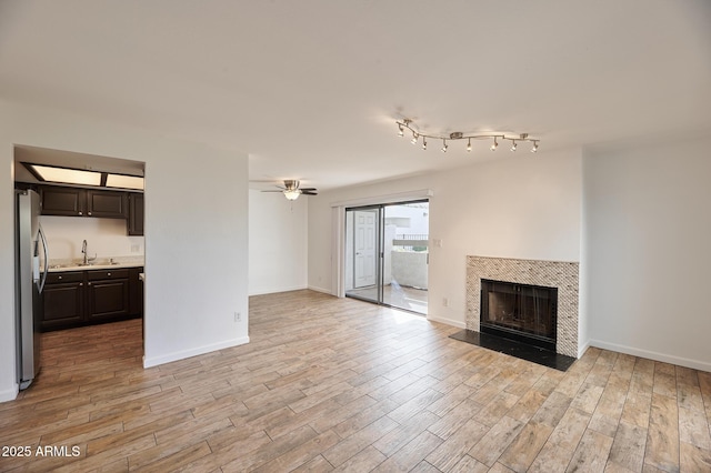 unfurnished living room featuring ceiling fan, a tiled fireplace, sink, and light hardwood / wood-style flooring