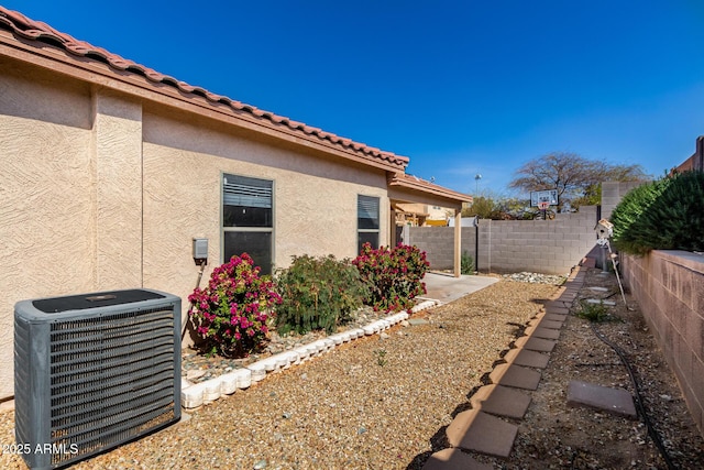 view of home's exterior with a tile roof, fence, central AC, and stucco siding