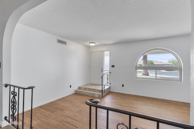 entrance foyer with arched walkways, visible vents, a textured ceiling, wood finished floors, and baseboards