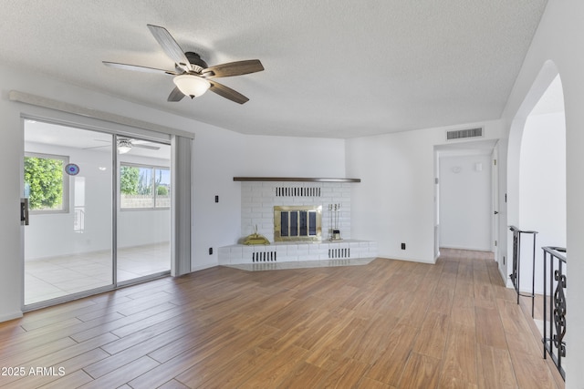 unfurnished living room featuring a textured ceiling, a brick fireplace, wood finished floors, and visible vents