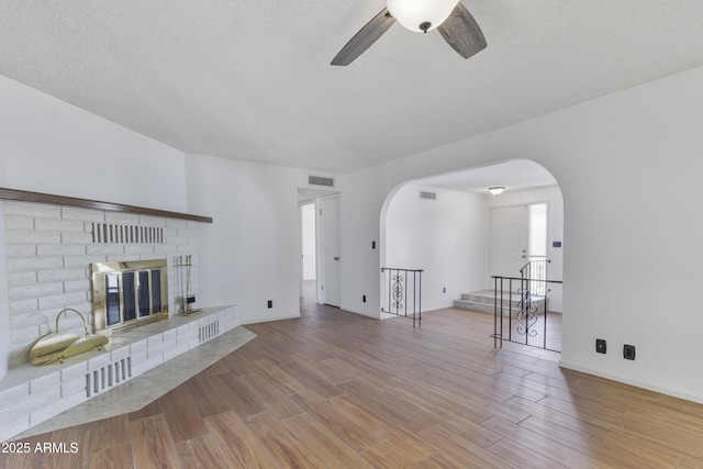 unfurnished living room featuring arched walkways, visible vents, a fireplace, and wood finished floors