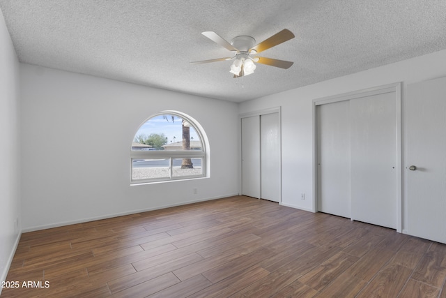 unfurnished bedroom with a textured ceiling, wood finished floors, two closets, and baseboards