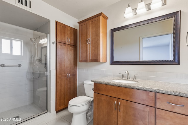 bathroom featuring toilet, tile patterned flooring, vanity, a shower stall, and tile walls