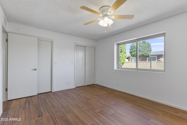 unfurnished bedroom featuring a textured ceiling, baseboards, two closets, and wood finished floors