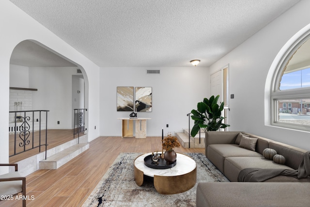 living area with light wood finished floors, visible vents, arched walkways, and a textured ceiling