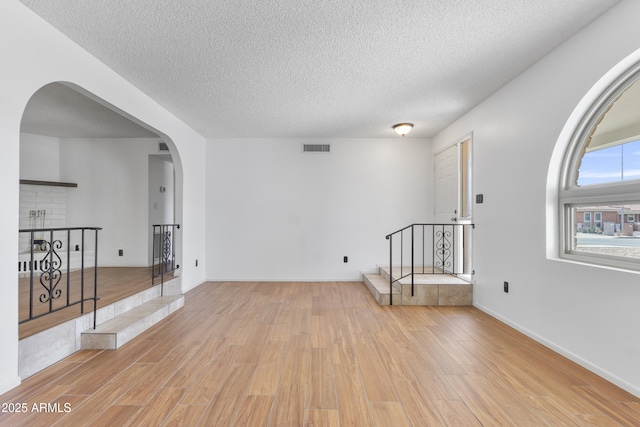 empty room featuring arched walkways, visible vents, a textured ceiling, wood finished floors, and baseboards