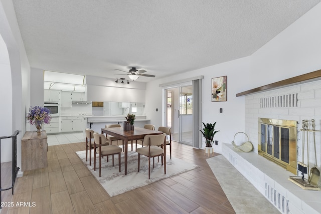 dining space with a textured ceiling, ceiling fan, wood finish floors, and a fireplace