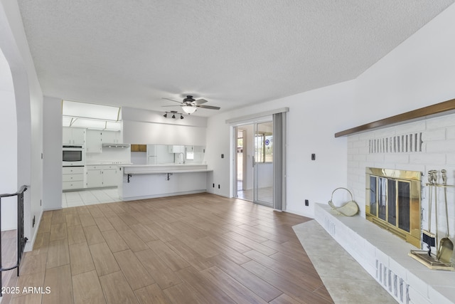 unfurnished living room with a textured ceiling, ceiling fan, a fireplace, and light wood-style floors