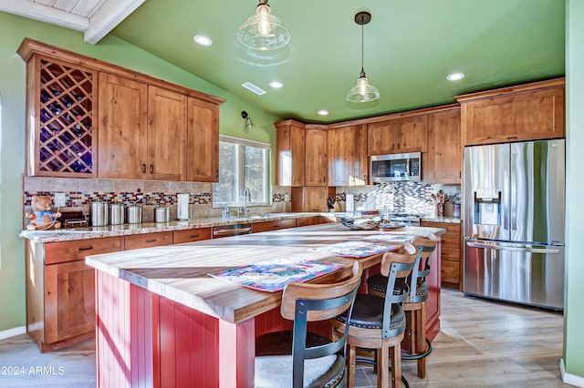 kitchen featuring a center island, lofted ceiling with beams, hanging light fixtures, light wood-type flooring, and appliances with stainless steel finishes