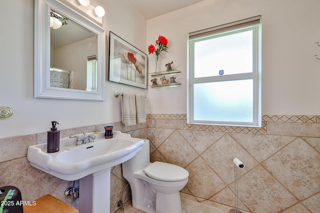 bathroom featuring wainscoting, tile walls, and toilet