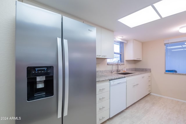 kitchen with light stone countertops, dishwasher, sink, stainless steel fridge, and white cabinets