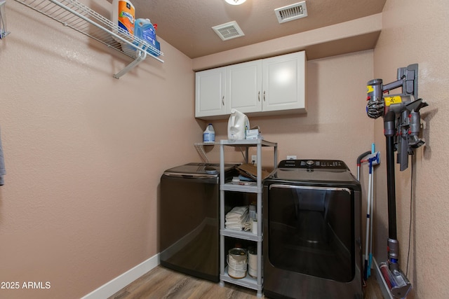 laundry room featuring light wood-type flooring, a textured ceiling, cabinets, and independent washer and dryer