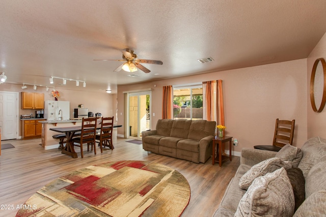 living room with rail lighting, light wood-type flooring, a textured ceiling, and ceiling fan