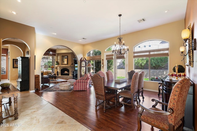 dining area featuring a notable chandelier, a stone fireplace, and light wood-type flooring