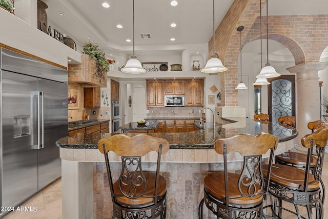 kitchen with backsplash, appliances with stainless steel finishes, decorative light fixtures, and a kitchen bar