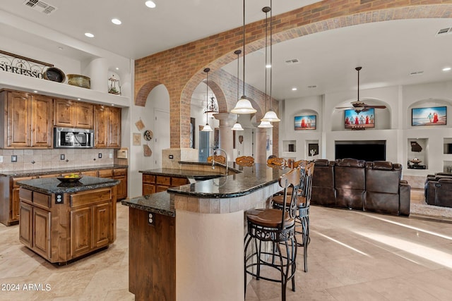 kitchen with backsplash, hanging light fixtures, ceiling fan, a large island, and dark stone countertops