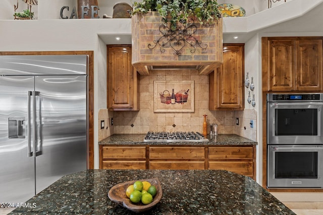 kitchen featuring appliances with stainless steel finishes, backsplash, custom range hood, and dark stone countertops