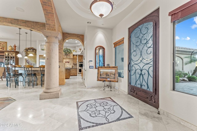 entrance foyer featuring ornate columns, light tile floors, and a raised ceiling