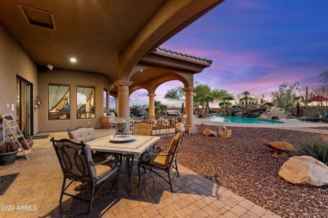 patio terrace at dusk featuring a fenced in pool