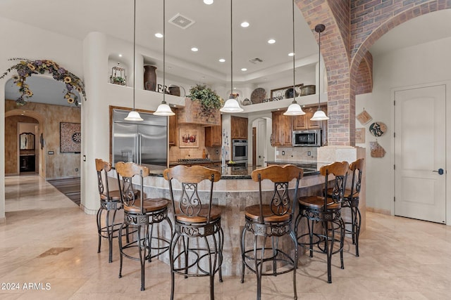 kitchen featuring decorative light fixtures, appliances with stainless steel finishes, light tile floors, a breakfast bar area, and tasteful backsplash