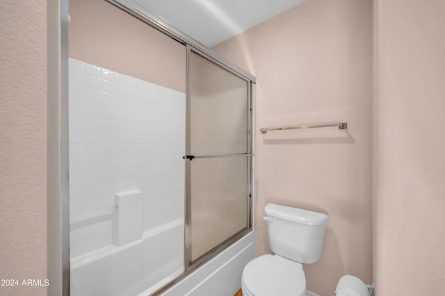 bathroom featuring toilet and bath / shower combo with glass door