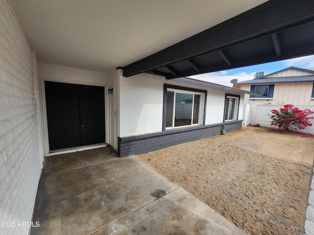 view of exterior entry with a patio, stucco siding, and fence