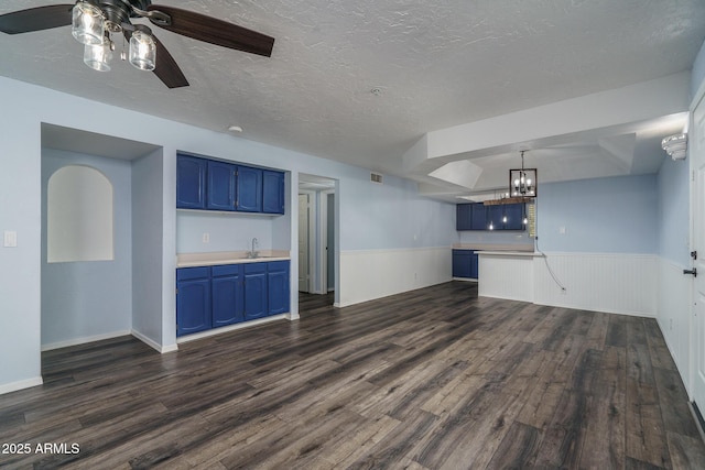 unfurnished living room featuring sink, a raised ceiling, dark hardwood / wood-style flooring, a textured ceiling, and ceiling fan with notable chandelier