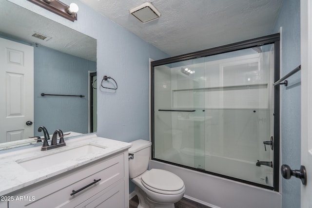 full bathroom with shower / bath combination with glass door, vanity, a textured ceiling, and toilet