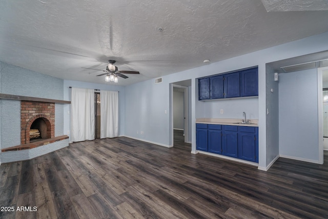 unfurnished living room with a textured ceiling, dark hardwood / wood-style floors, sink, and a brick fireplace