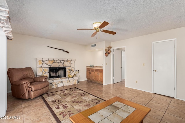 tiled living room with ceiling fan, a fireplace, and a textured ceiling