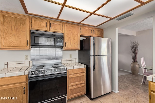 kitchen featuring tile countertops, tasteful backsplash, stainless steel fridge, light tile patterned floors, and electric stove