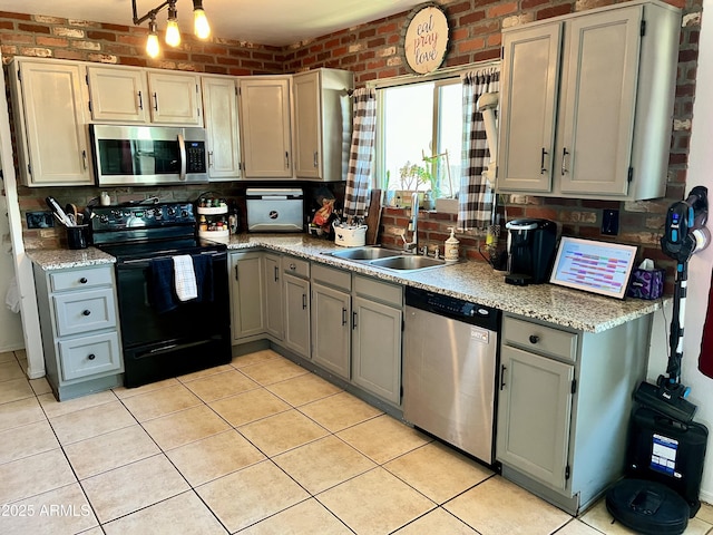 kitchen with light tile patterned floors, sink, stainless steel appliances, and brick wall