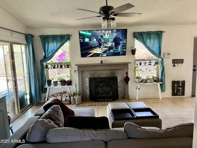 living room with a tile fireplace, ceiling fan, tile patterned flooring, a textured ceiling, and vaulted ceiling