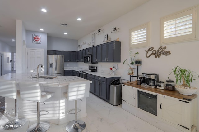 kitchen with light stone counters, sink, a breakfast bar area, and appliances with stainless steel finishes