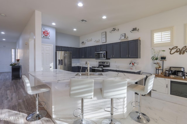 kitchen featuring a large island, appliances with stainless steel finishes, a kitchen bar, and light stone countertops