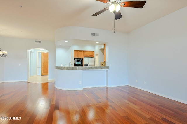 unfurnished living room featuring sink, ceiling fan with notable chandelier, and light wood-type flooring