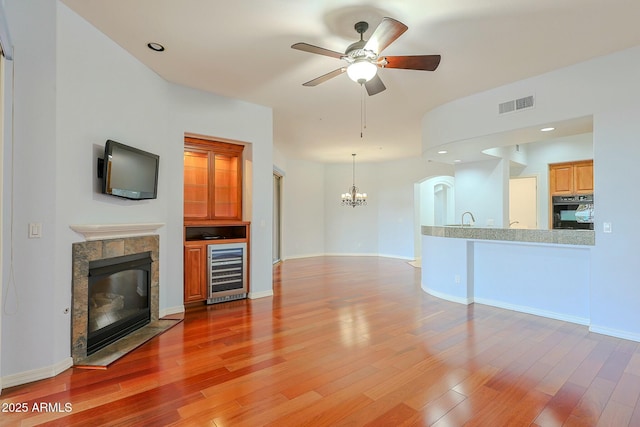 unfurnished living room with hardwood / wood-style flooring, ceiling fan with notable chandelier, a tile fireplace, and beverage cooler