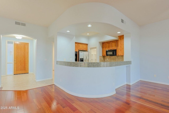 kitchen featuring tasteful backsplash, stainless steel fridge, light hardwood / wood-style floors, and kitchen peninsula