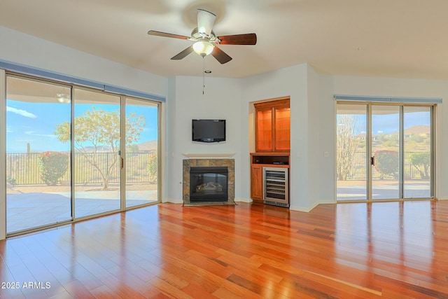 unfurnished living room featuring a premium fireplace, wine cooler, ceiling fan, and light hardwood / wood-style flooring