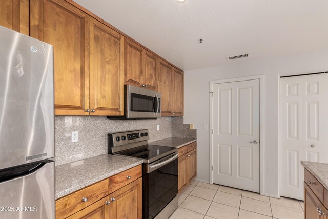 11260 N 92nd St Unit 2102, Scottsdale, AZ 85260 - kitchen featuring appliances with stainless steel finishes, brown cabinetry, light tile patterned floors, and decorative backsplash