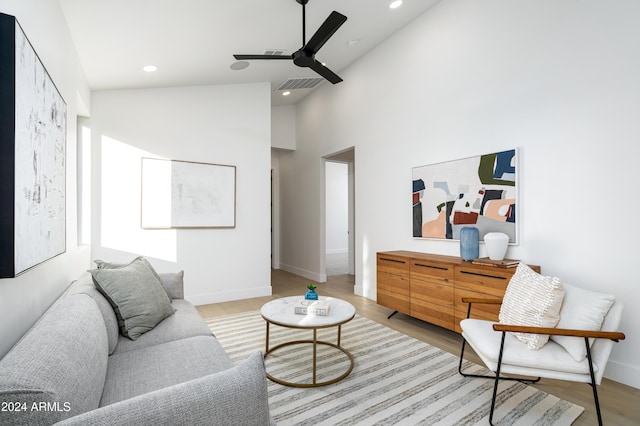 living room with ceiling fan, a towering ceiling, and light wood-type flooring