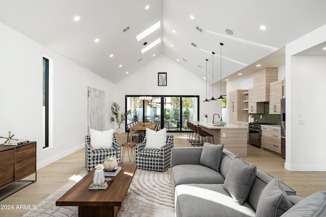 living room with high vaulted ceiling, a skylight, light hardwood / wood-style flooring, and sink