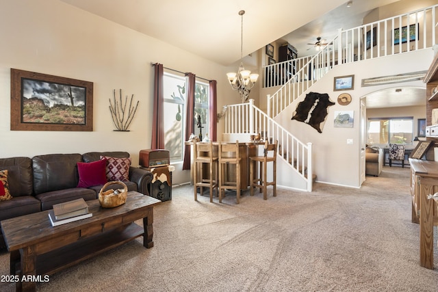 carpeted living room featuring ceiling fan with notable chandelier and a high ceiling