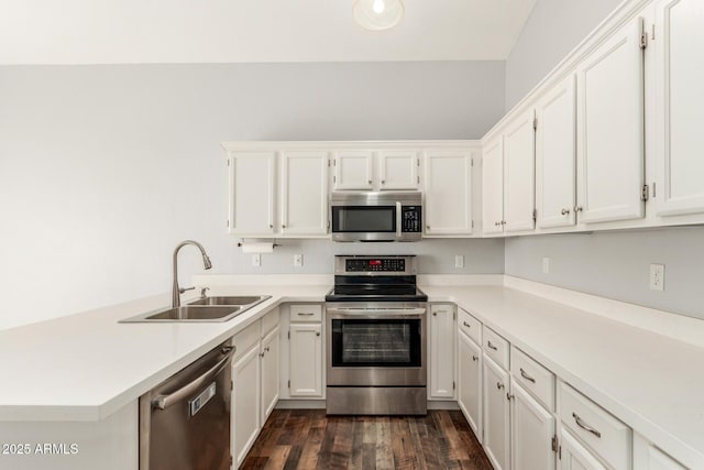 kitchen with dark wood-style floors, stainless steel appliances, light countertops, a sink, and a peninsula