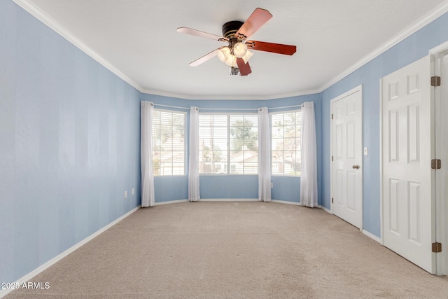 carpeted spare room featuring baseboards, ornamental molding, and a ceiling fan