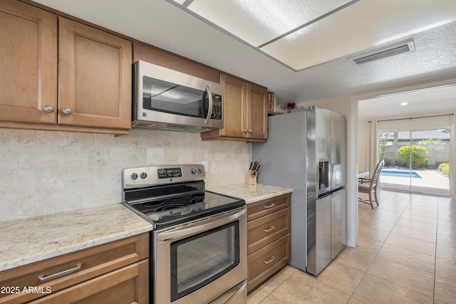kitchen with brown cabinets, visible vents, tasteful backsplash, and stainless steel appliances