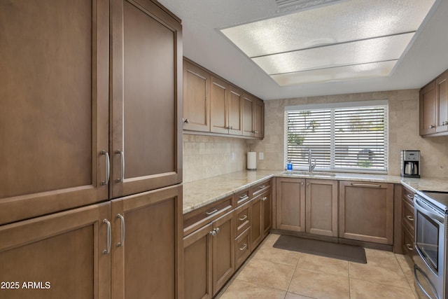 kitchen featuring light tile patterned floors, a sink, decorative backsplash, electric range, and light stone counters