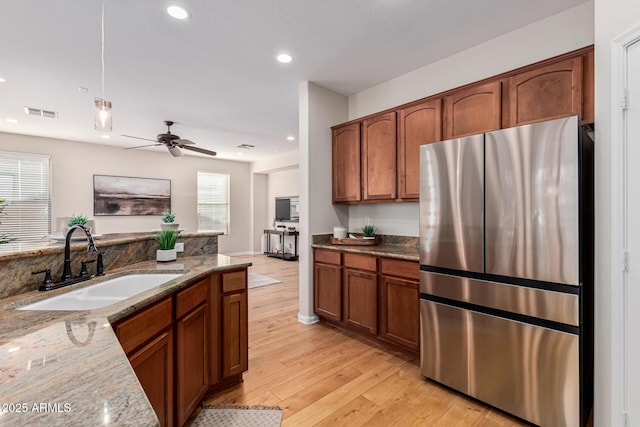 kitchen with light stone countertops, stainless steel fridge, ceiling fan, sink, and pendant lighting