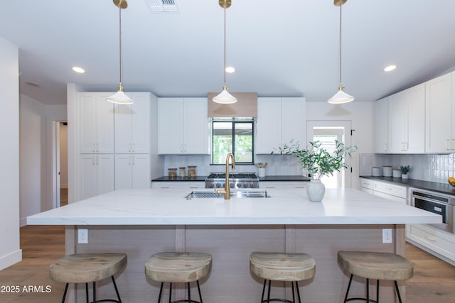 kitchen with tasteful backsplash, a sink, white cabinets, a breakfast bar area, and light wood finished floors