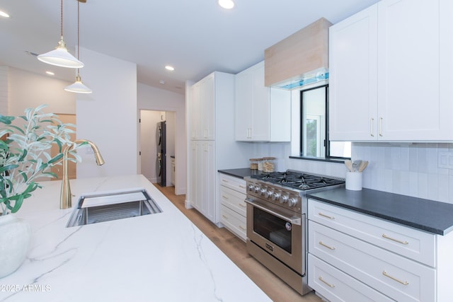 kitchen featuring stainless steel range, a sink, white cabinetry, recessed lighting, and hanging light fixtures